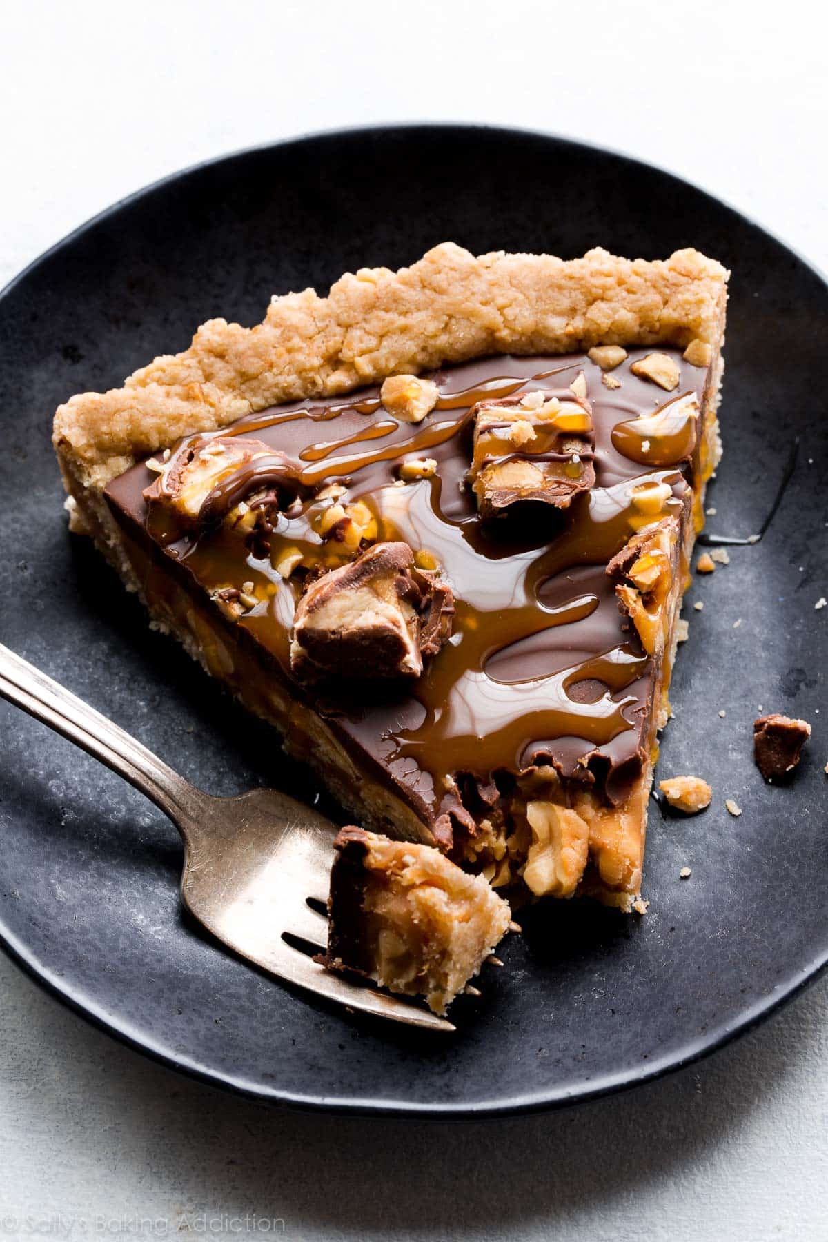 Snickers caramel tart with salted caramel, peanut crust, salty peanuts, and chocolate peanut butter topping! Recipe on sallysbakingaddiction.com