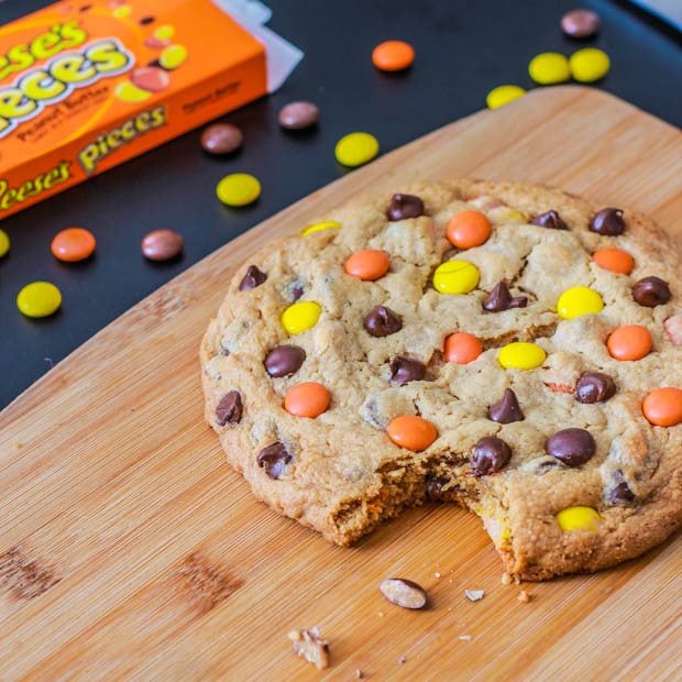 one giant peanut butter Reese's Pieces cookie with a bite taken out of it on a wood board