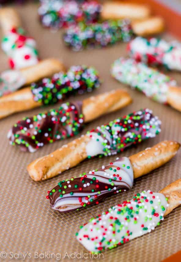 pretzels dipped in chocolate and topped with sprinkles on a silpat baking mat