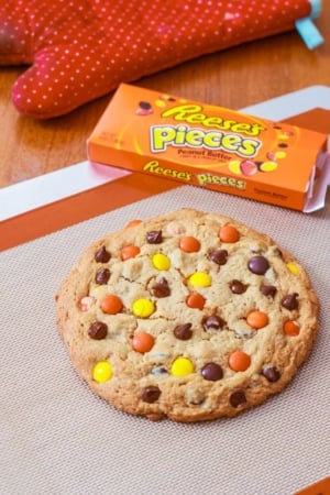 one giant peanut butter Reese's Pieces cookie on a silpat baking mat