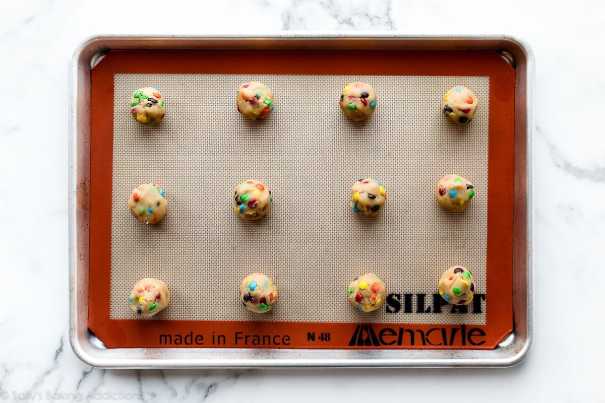 M&M cookie dough balls arranged on a lined baking sheet