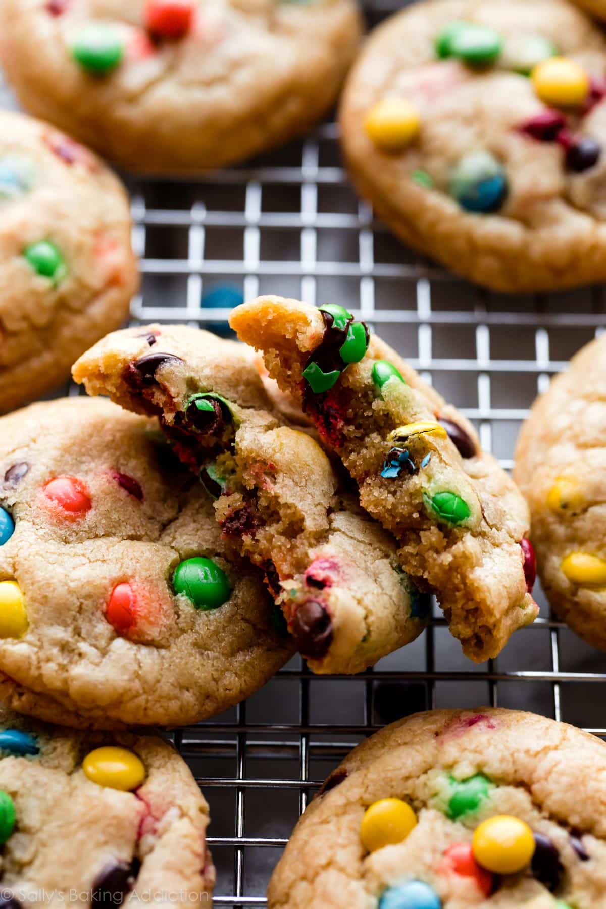 close-up photo of m&m cookies on a cooling rack with one broken in half