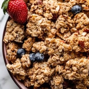 granola clusters in pink bowl with strawberry and blueberries.
