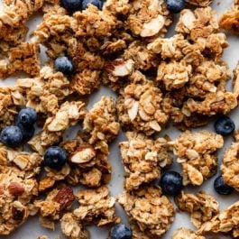 clusters of maple almond granola spread out with blueberries dotted all over.