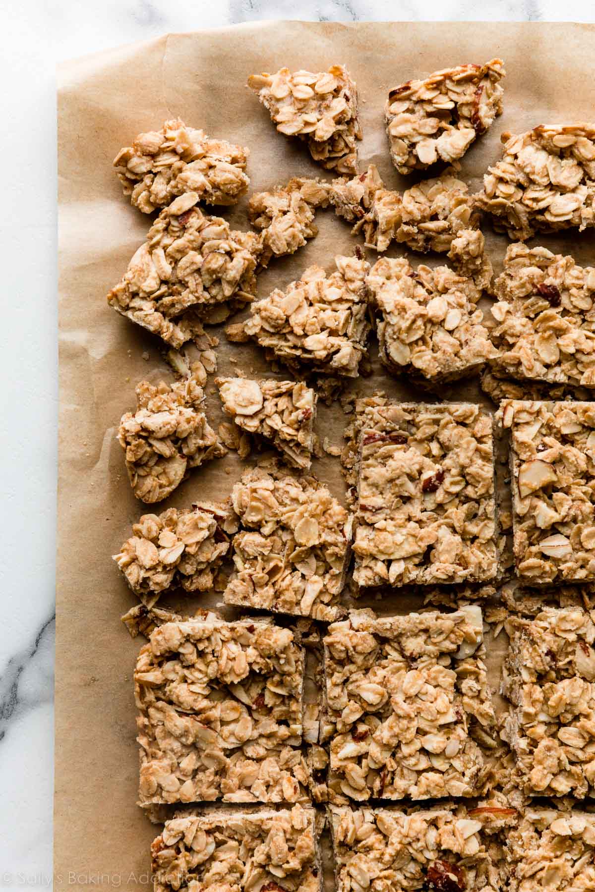 bars of granola mixture in squares and broken into chunks on brown parchment paper.