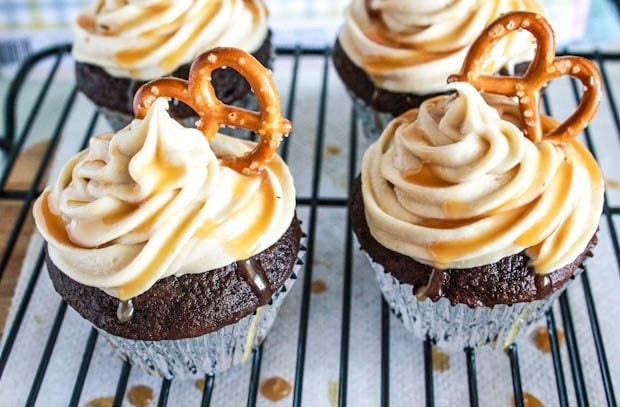 chocolate cupcakes topped with salted caramel frosting and a pretzel on a cooling rack