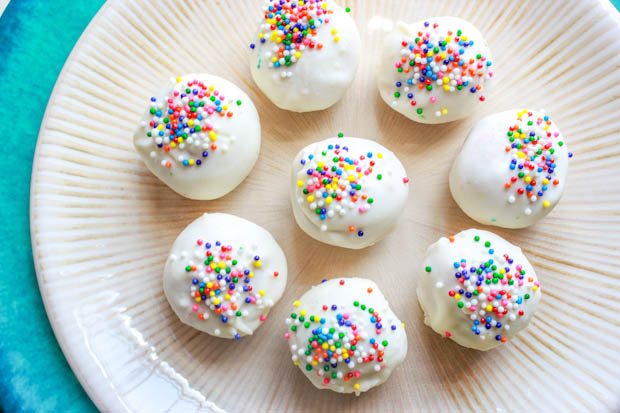 overhead image of golden Oreo truffles coated in white chocolate with sprinkles on a cream plate