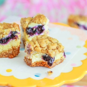 blueberry lemon cheesecake bars on a yellow cake stand
