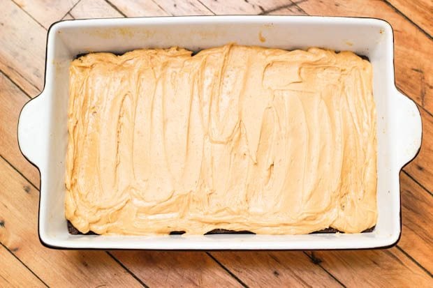 peanut butter frosting spread on top of brownies in a baking dish