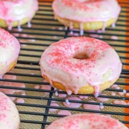 strawberry frosted donuts with pink sugar on a cooling rack