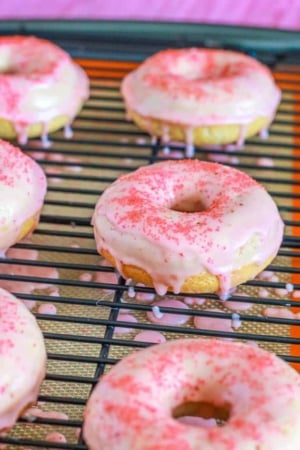 strawberry frosted donuts with pink sugar on a cooling rack