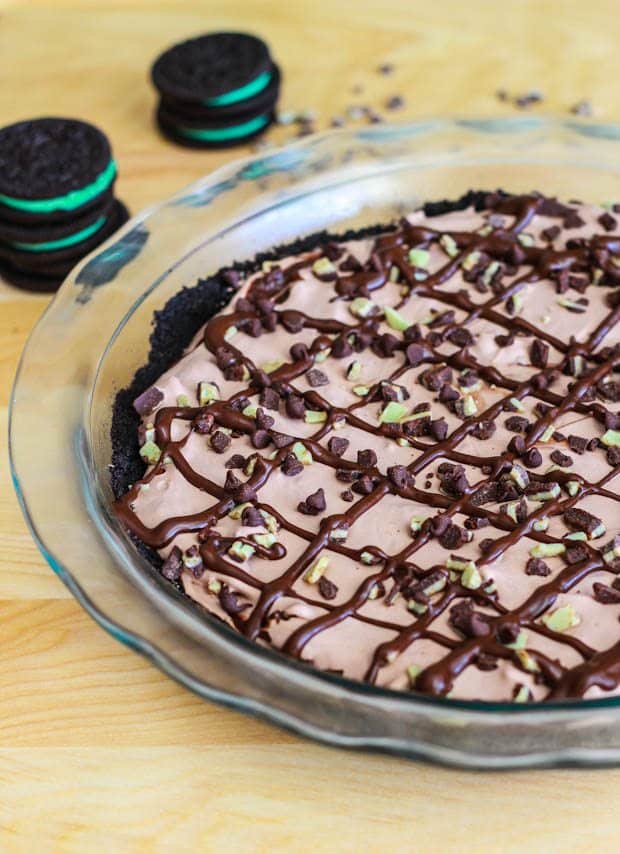 skinny frozen mint chocolate chip pie topped with chocolate syrup in a glass pie dish