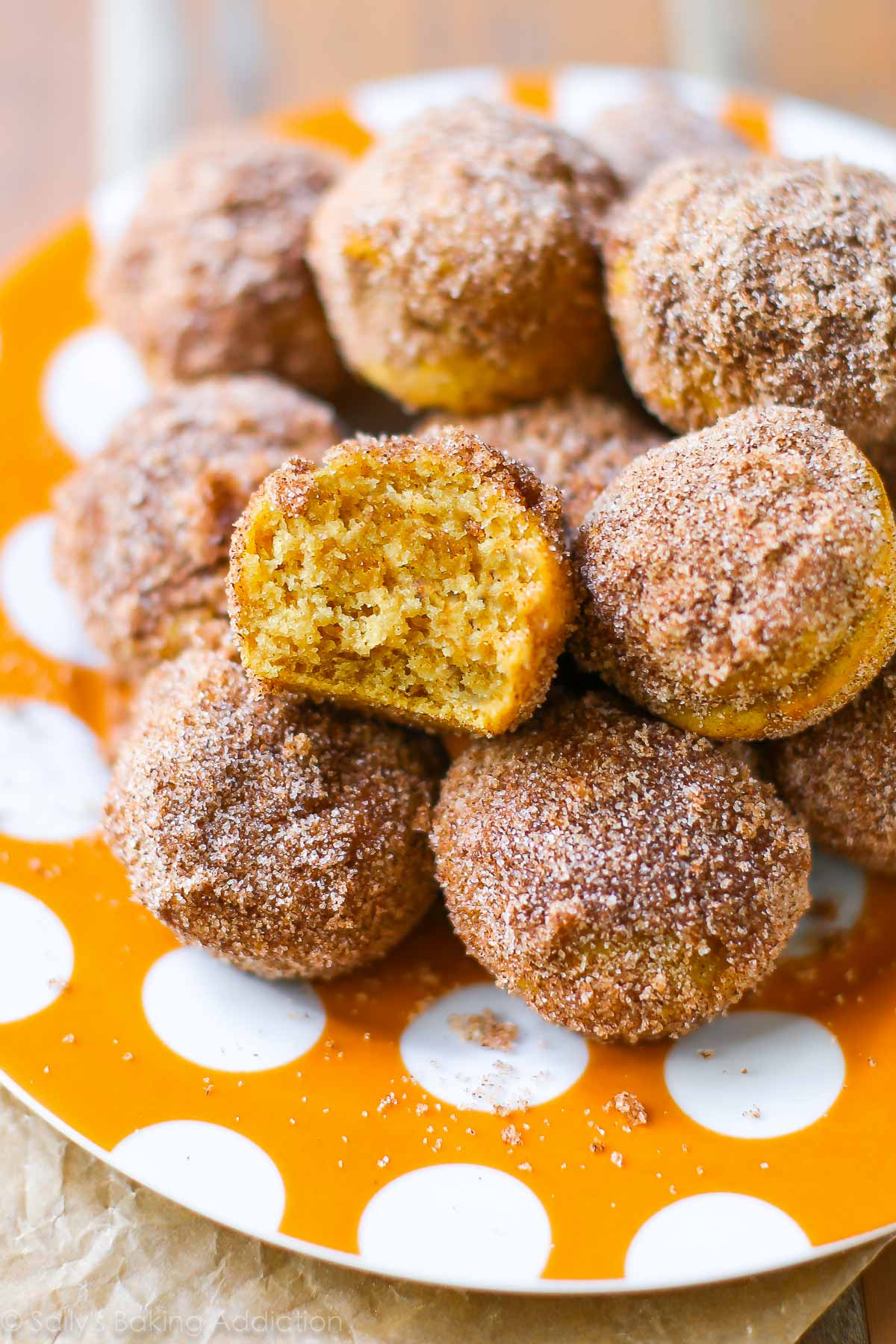 mini cinnamon sugar pumpkin muffins with a bite taken out of one showing the inside on an orange polka dot plate