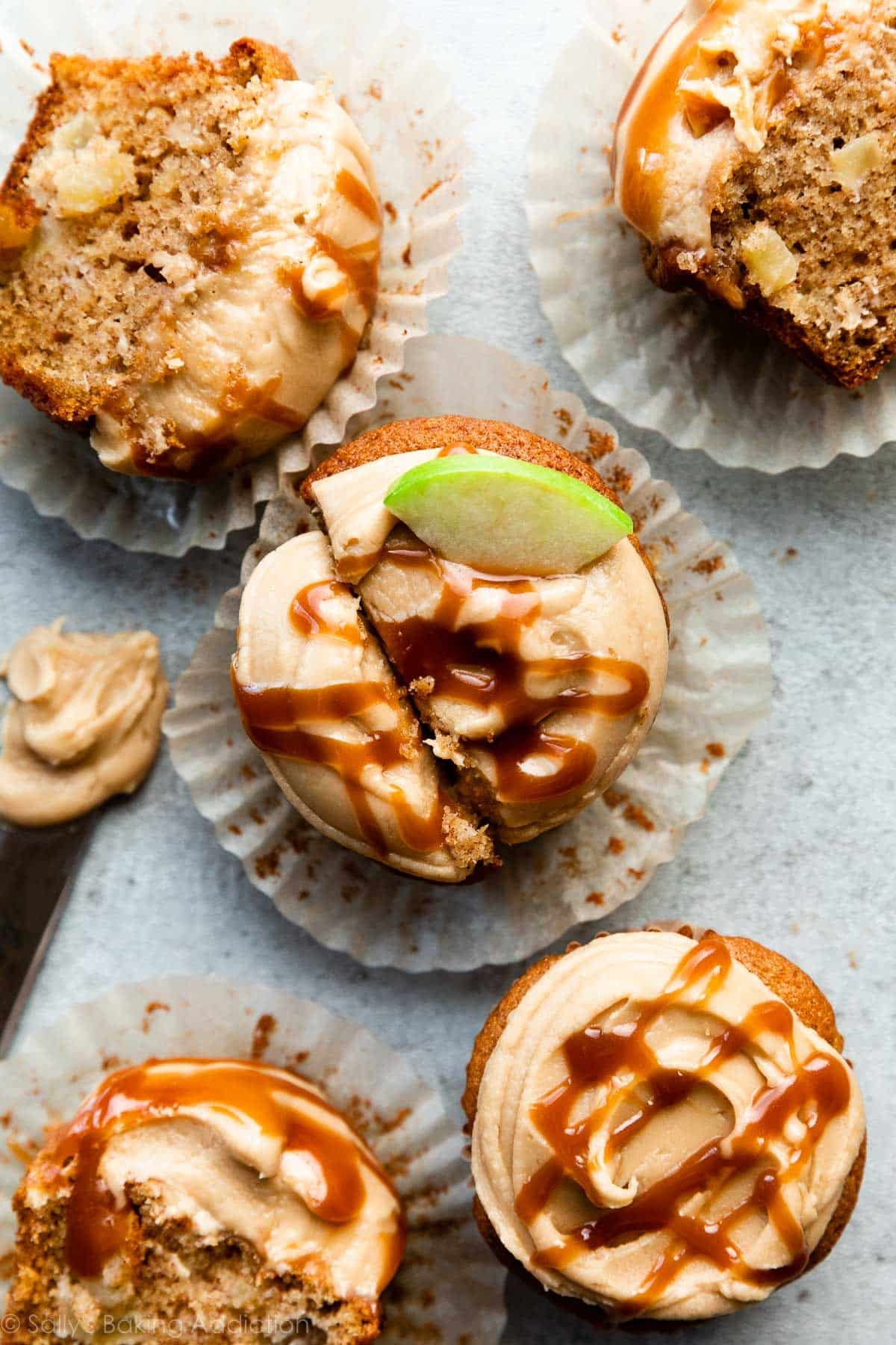 5 caramel apple cupcakes with salted caramel drizzled on top and a few cut in half.