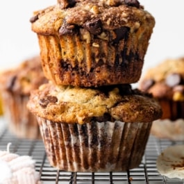 2 banana chocolate chip cinnamon streusel muffins stacked together on wire cooling rack.