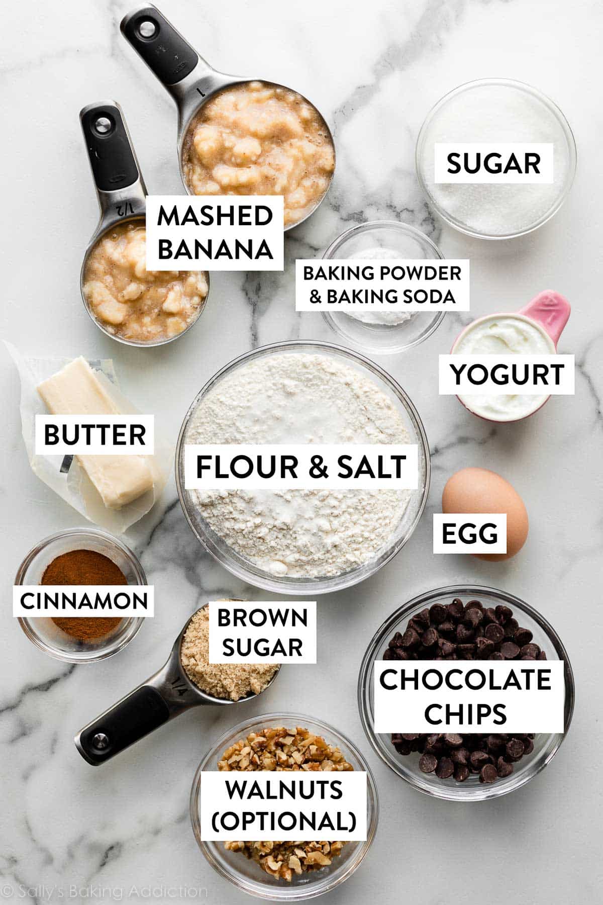flour, egg, yogurt, sugar, brown sugar, chocolate chips, butter, and other ingredients on marble counter.