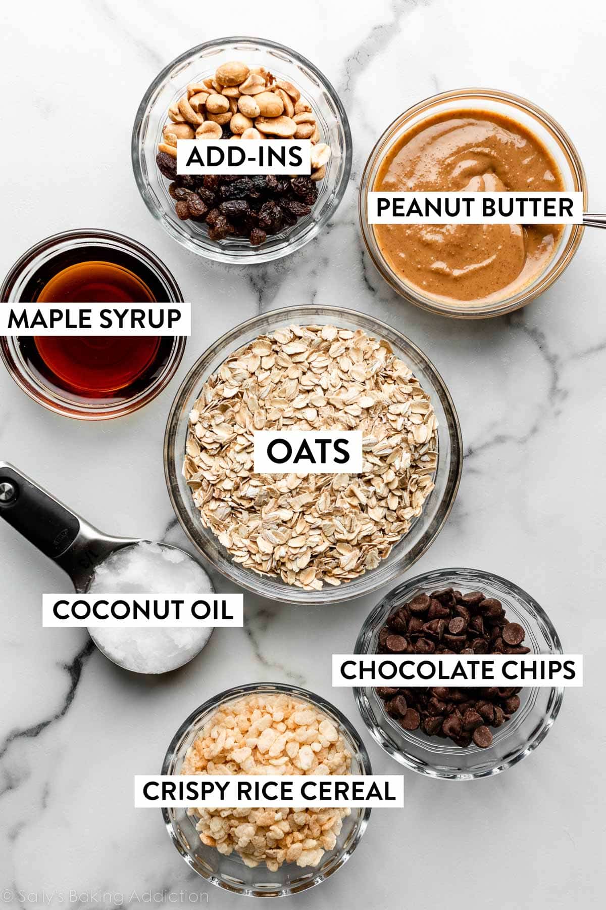 ingredients on counter including oats, maple syrup, peanut butter, coconut oil, chocolate chips, and more.