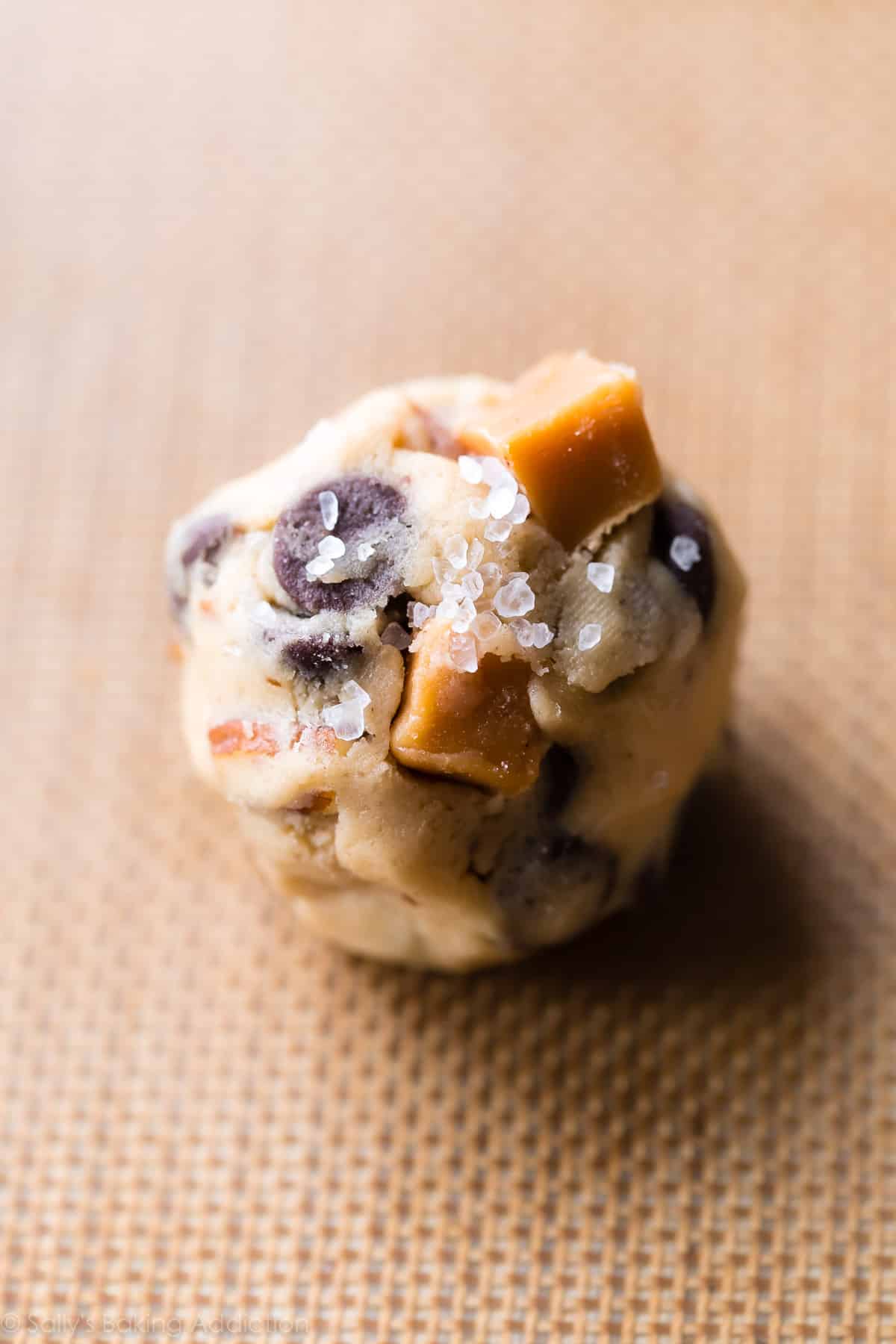 Caramel chocolate chip cookie dough ball on a baking sheet before baking