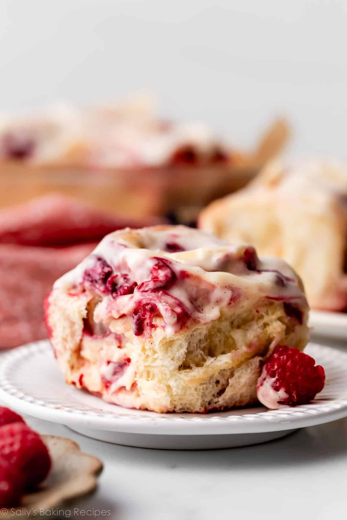 raspberry sweet roll with cream cheese icing on white plate.