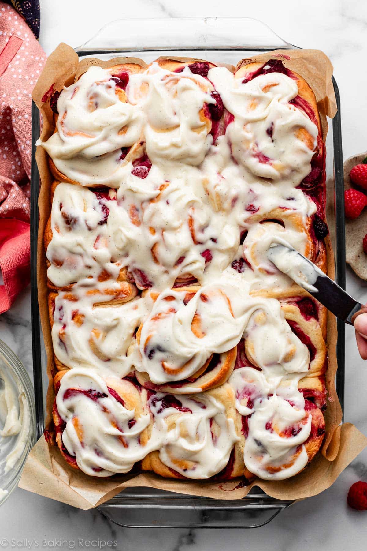 glass pan of raspberry sweet rolls with cream cheese icing.