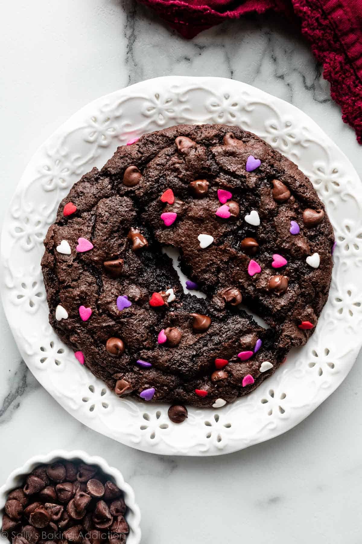 giant chocolate cookie with heart sprinkles on white plate on marble counter.