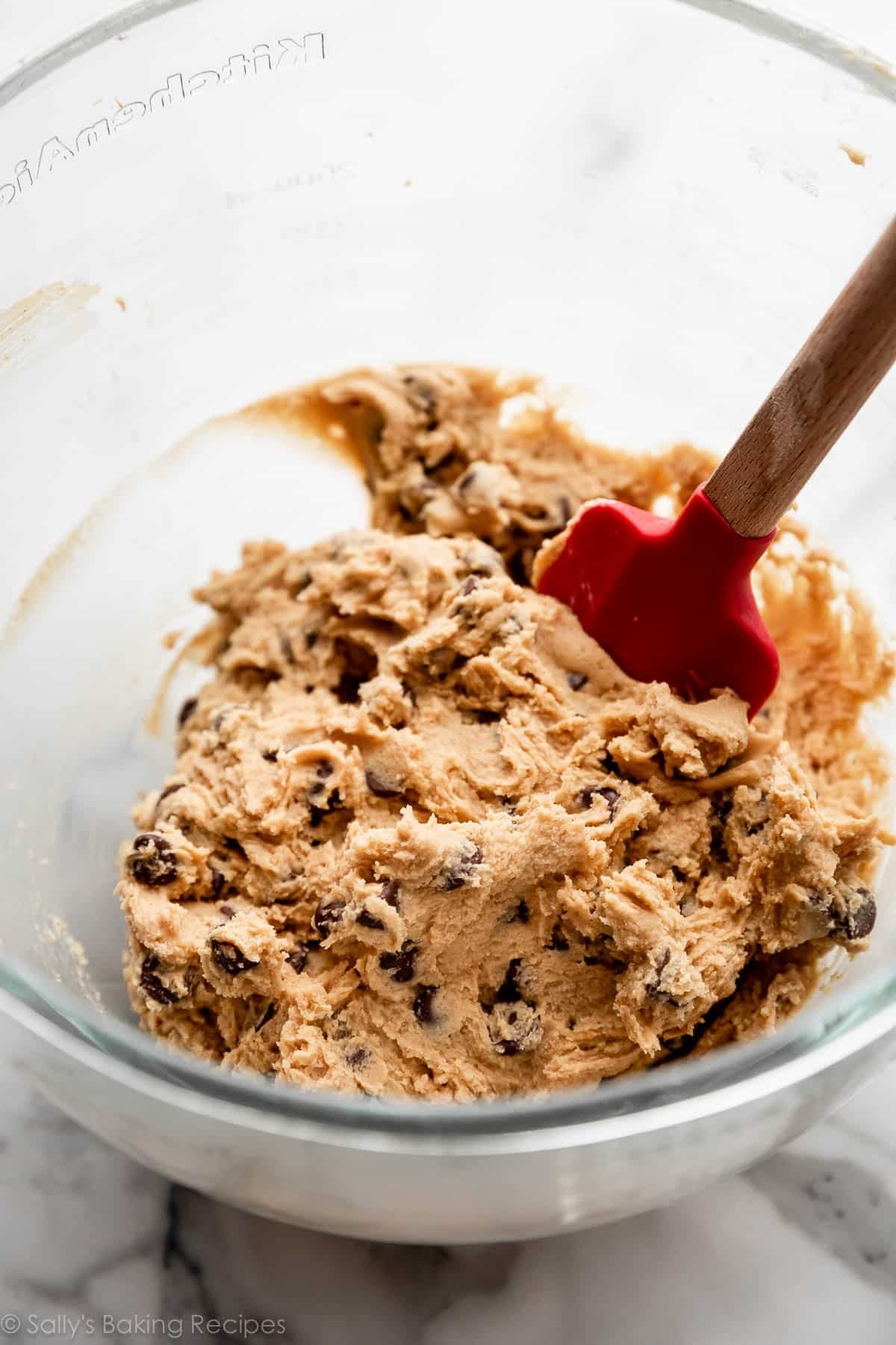 peanut butter chocolate chip cookie dough with red spatula in glass mixing bowl.