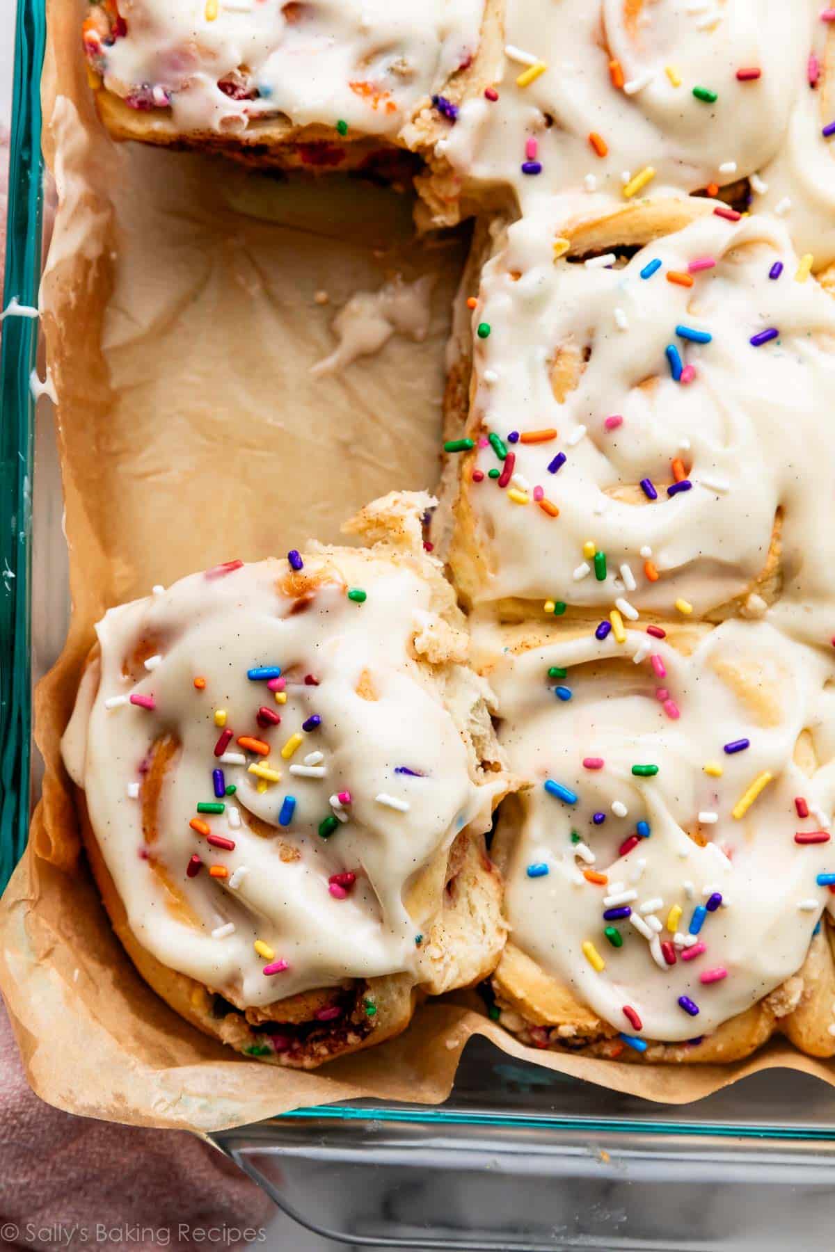 birthday cake cinnamon rolls with icing in parchment paper-lined pan.