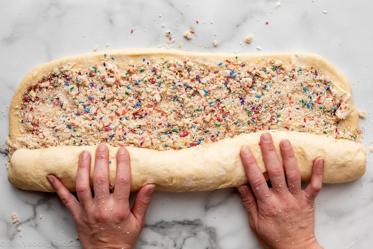 hands rolling up dough with sprinkle filling.