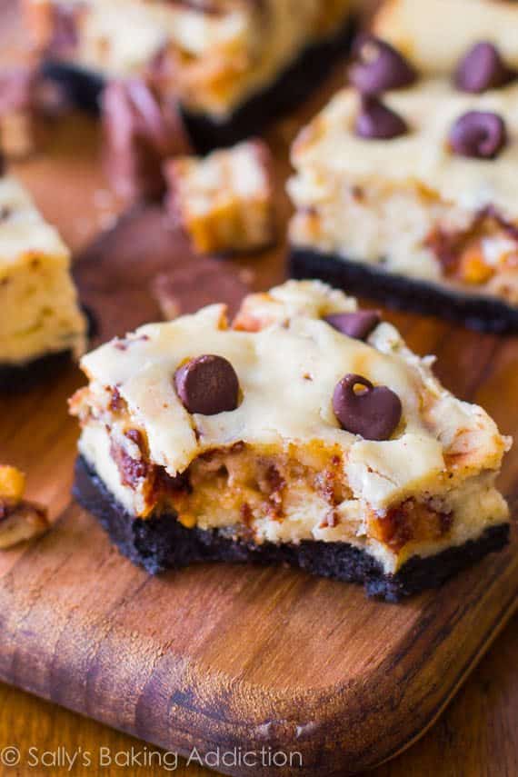 Snickers cheesecake bars on a wood board with a bite taken from one