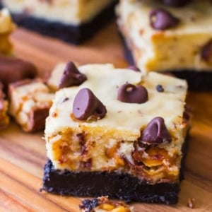 Snickers cheesecake bars on a wood board