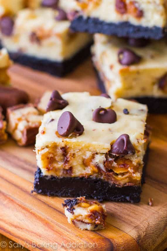 Snickers cheesecake bars on a wood board