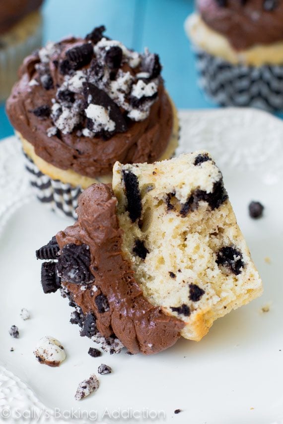 cookies and cream cupcakes topped with chocolate frosting and crushed Oreos with one cut in half showing the inside of the cupcake