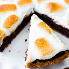 s'mores brownie pie on a white serving platter with a slice cut and placed on the serving platter