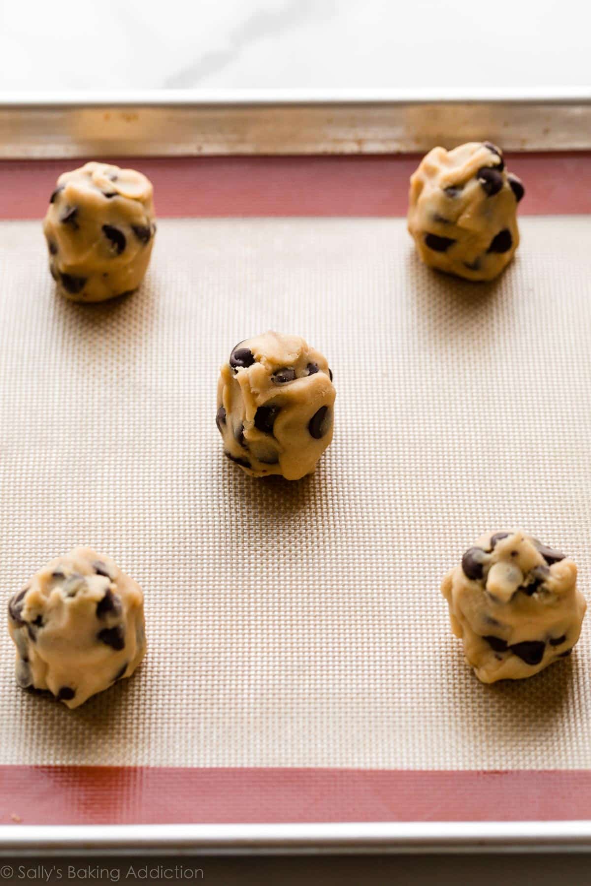 cookie dough balls shown on a silicone baking mat lined baking sheet