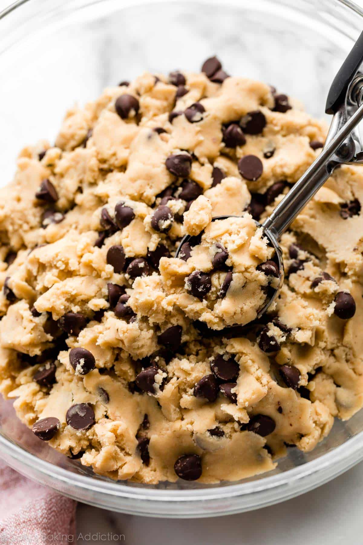 scooping chocolate chip cookie dough out of a glass bowl with a cookie scoop