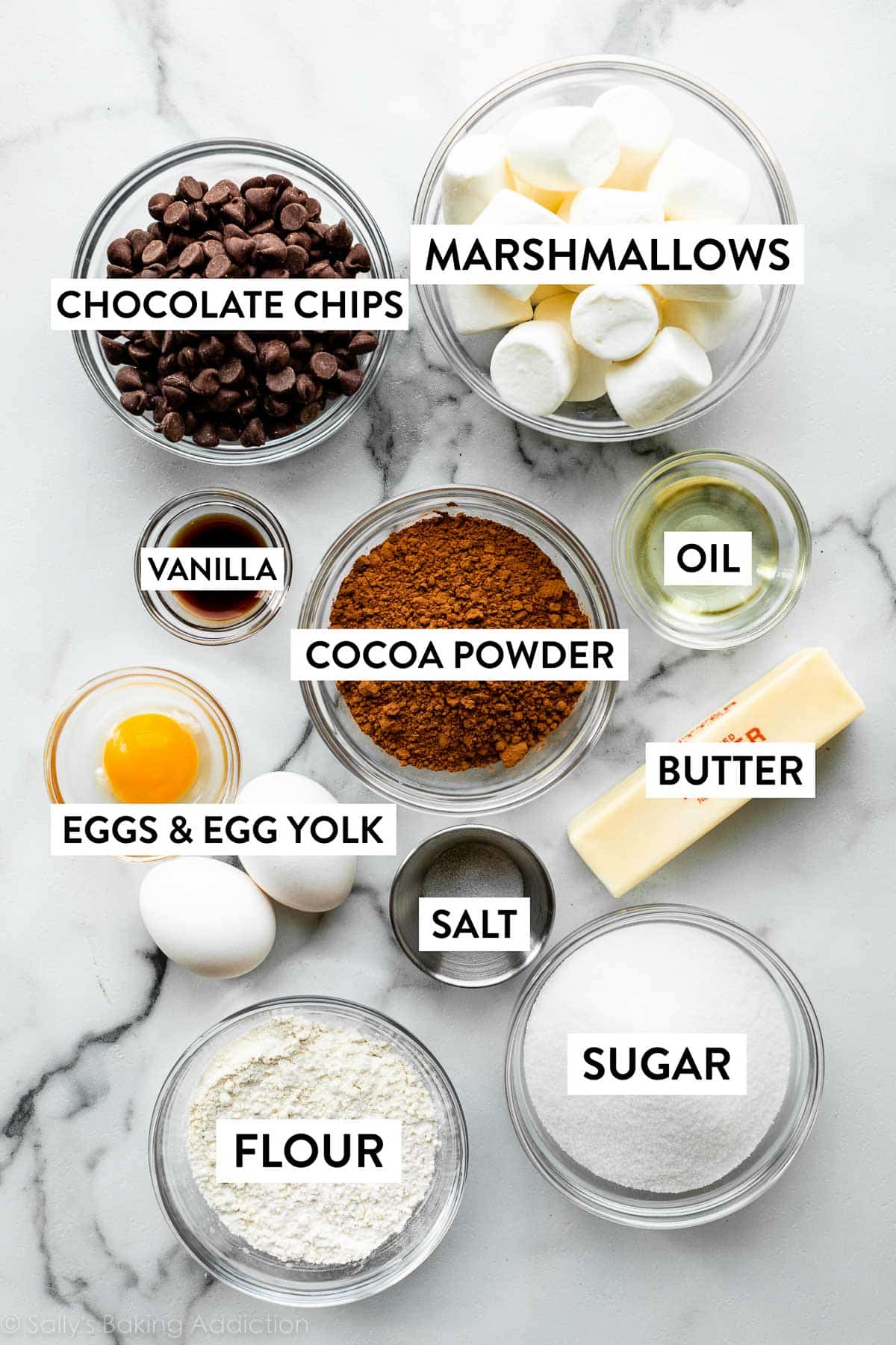 ingredients on marble counter including cocoa powder, oil, butter, sugar, flour, eggs, and chocolate chips.