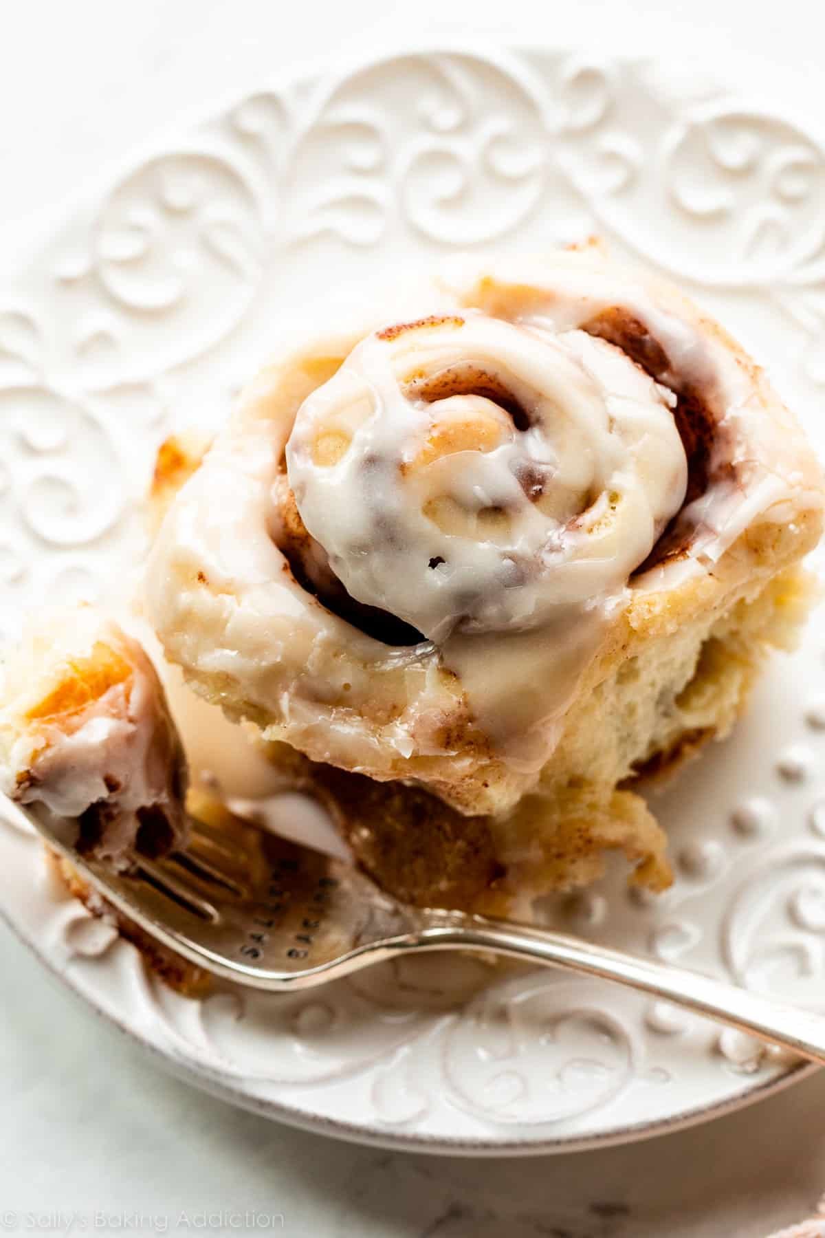 one cinnamon roll with icing on top on white plate.
