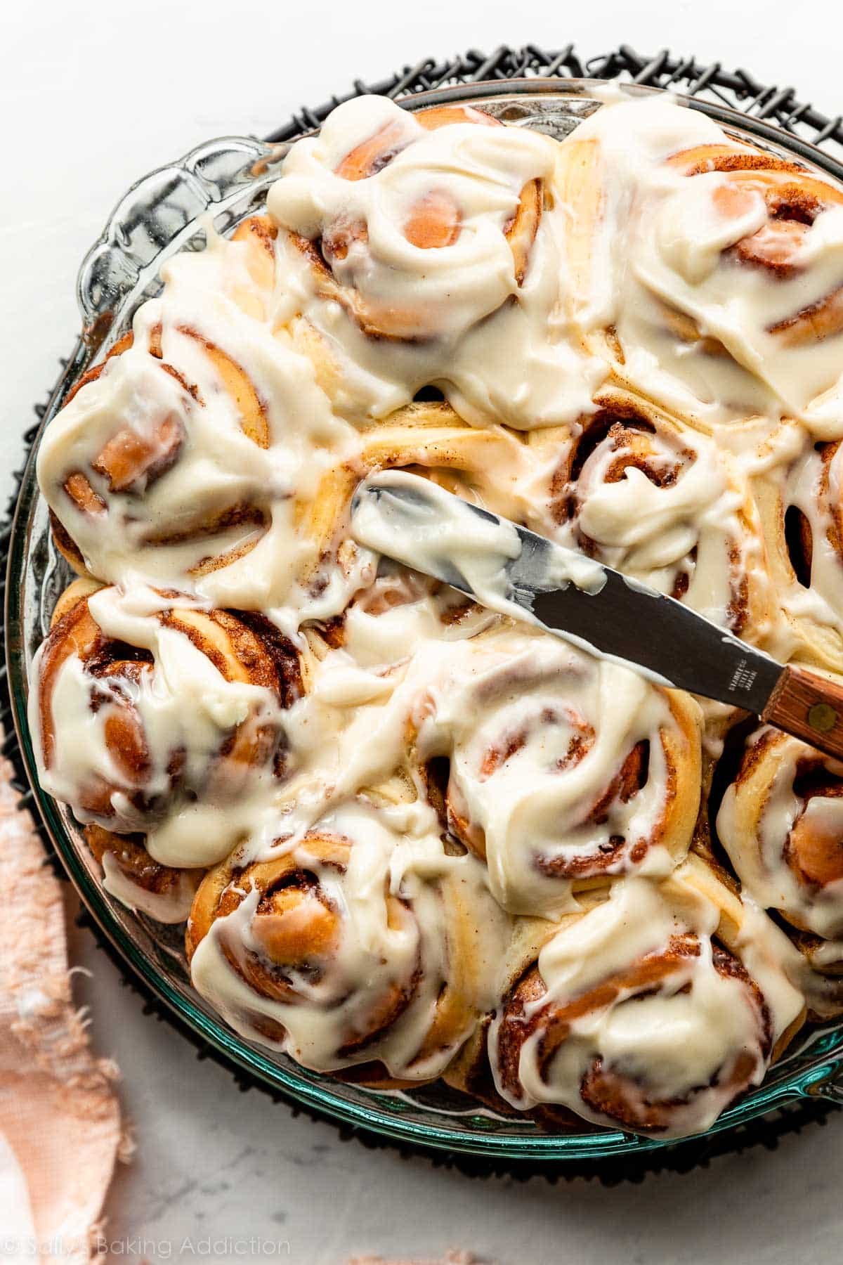 spreading frosting on cinnamon rolls in round dish.