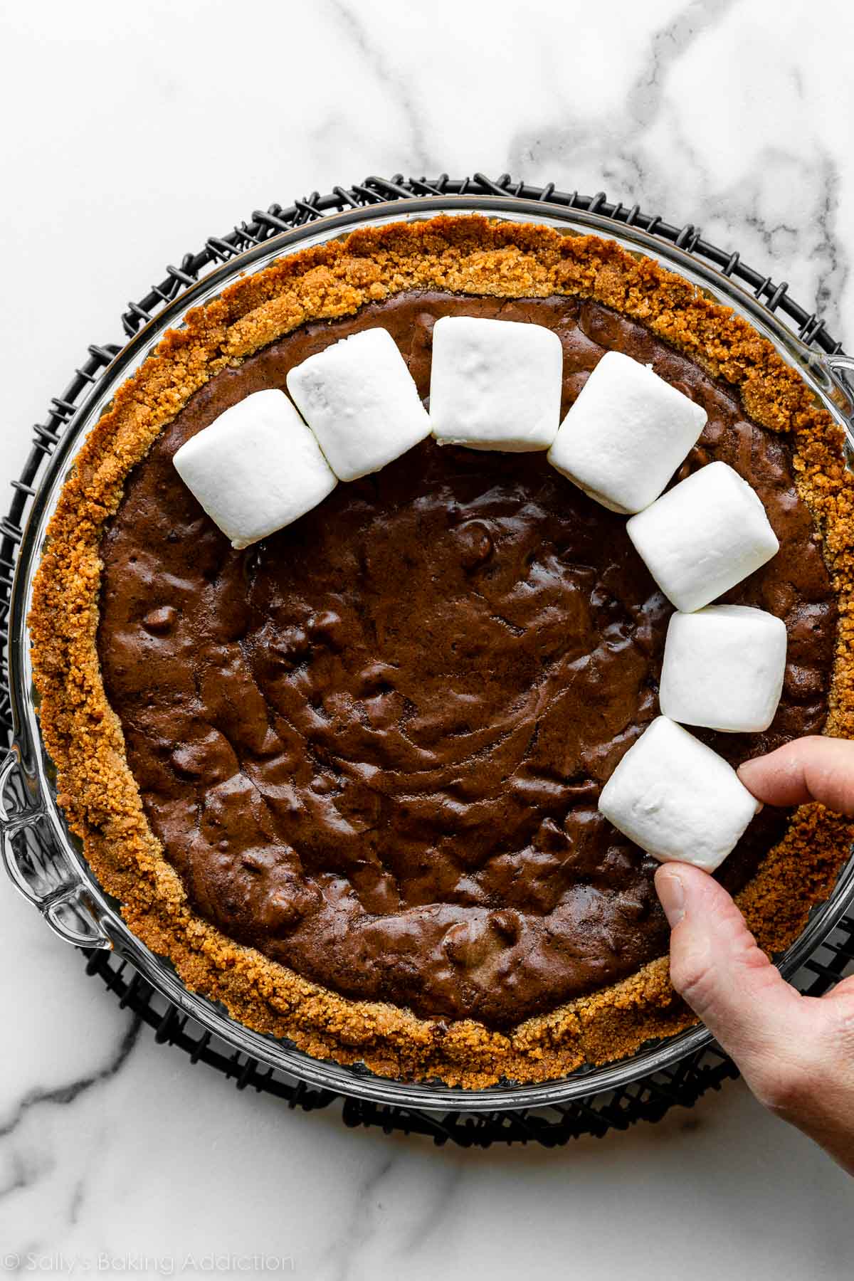 adding marshmallows on top of baked brownie pie with graham cracker crust.
