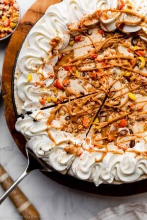 decorated peanut butter ice cream pie with Reese's Pieces, whipped cream, and peanut butter swirls on top.