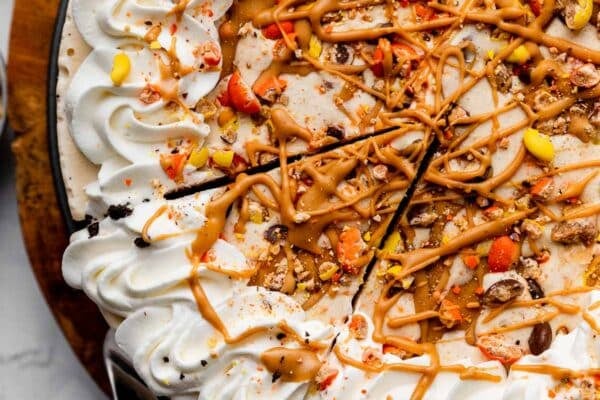 decorated peanut butter ice cream pie with Reese's Pieces, whipped cream, and peanut butter swirls on top.