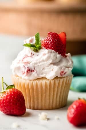 close-up of strawberry shortcake cupcake with whipped cream, mint, and fresh strawberry slices on top.