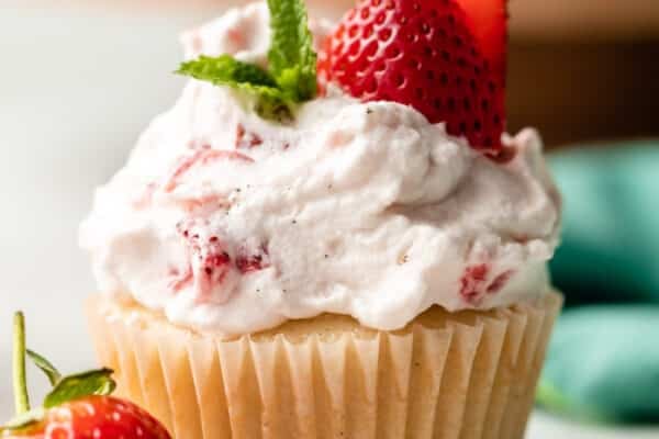 close-up of strawberry shortcake cupcake with whipped cream, mint, and fresh strawberry slices on top.