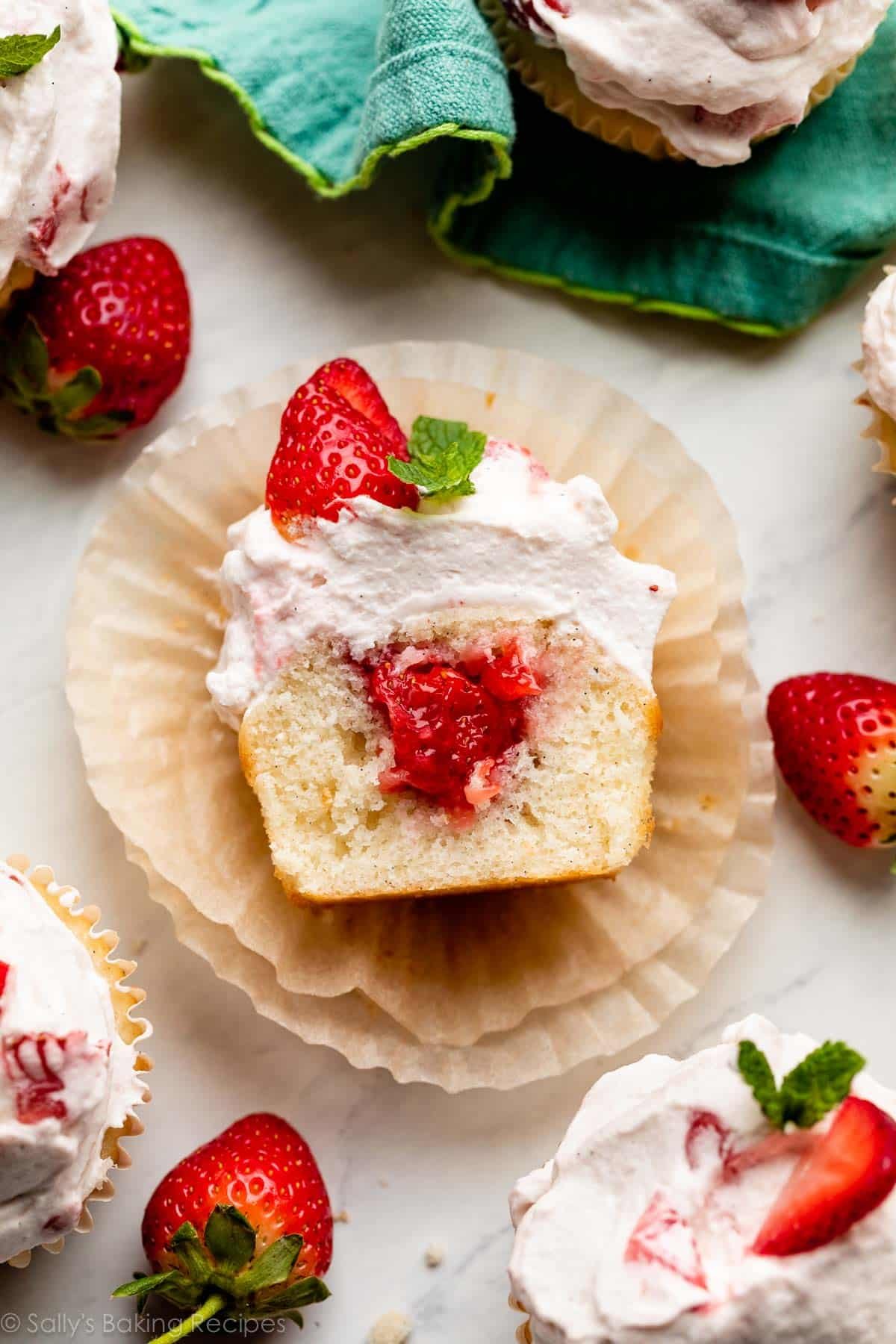 overhead photo of strawberry shortcake cupcake placed on cupcake wrappers and cut open to show filling.