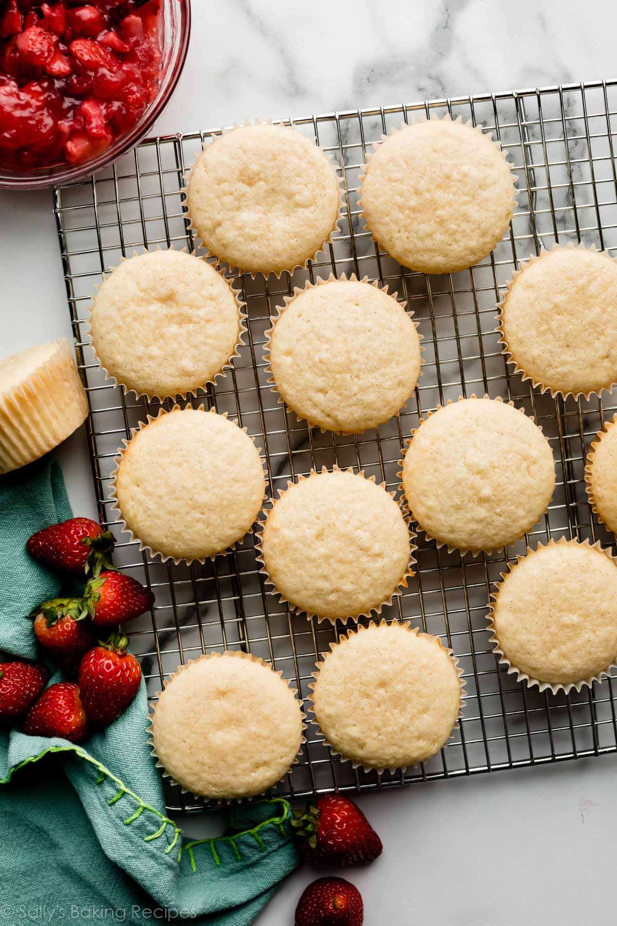 vanilla bean cupcakes on silver cooling rack with strawberries and blue linen napkin.