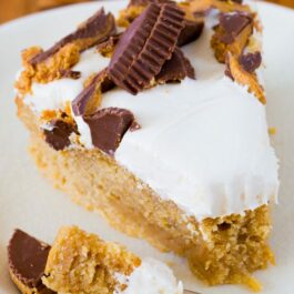 slice of peanut butter cake topped with marshmallow frosting and chopped peanut butter cups on a white plate with a fork