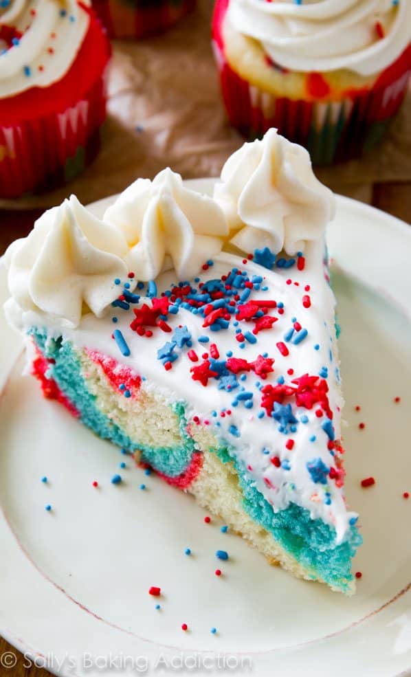 slice of red, white, and blue tie-dye cake topped with vanilla frosting and sprinkles on a white plate