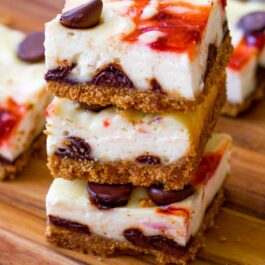 stack of 3 strawberry chocolate chip cheesecake bars on a wood board