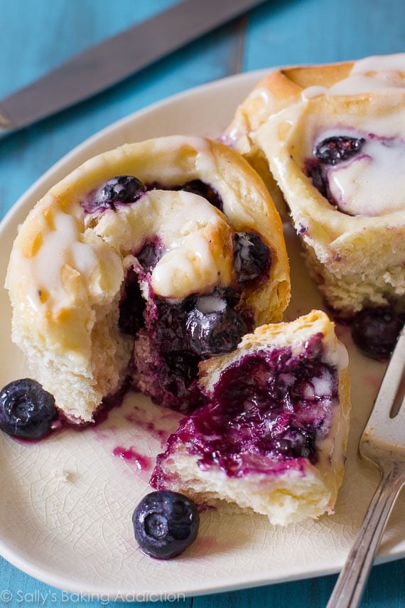 blueberry sweet rolls with lemon glaze on a cream plate with a fork