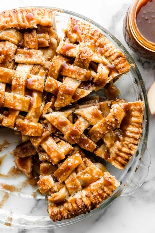 overhead photo of salted caramel apple pie slices with lattice pie crust in a glass pie dish.